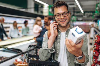 man on the phone in grocer store looking at a carton of food