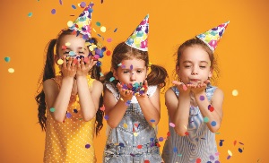 Three little girls in birthday hats blowing confetti away