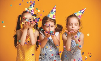 Three little girls in birthday hats blowing confetti away